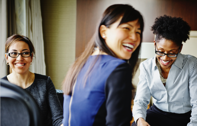 A group of career women smiling and working in a hotel suite.