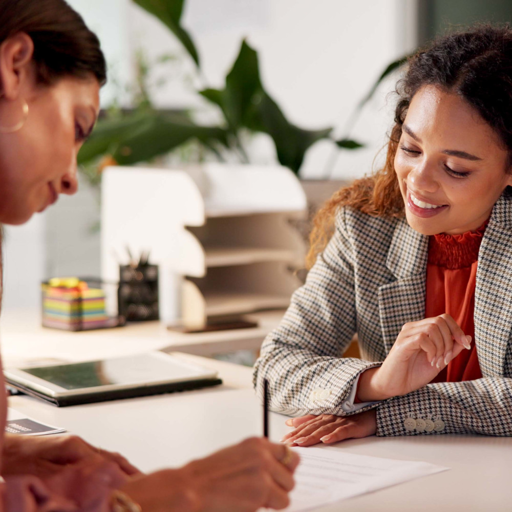 Woman signs paper while another woman smiles